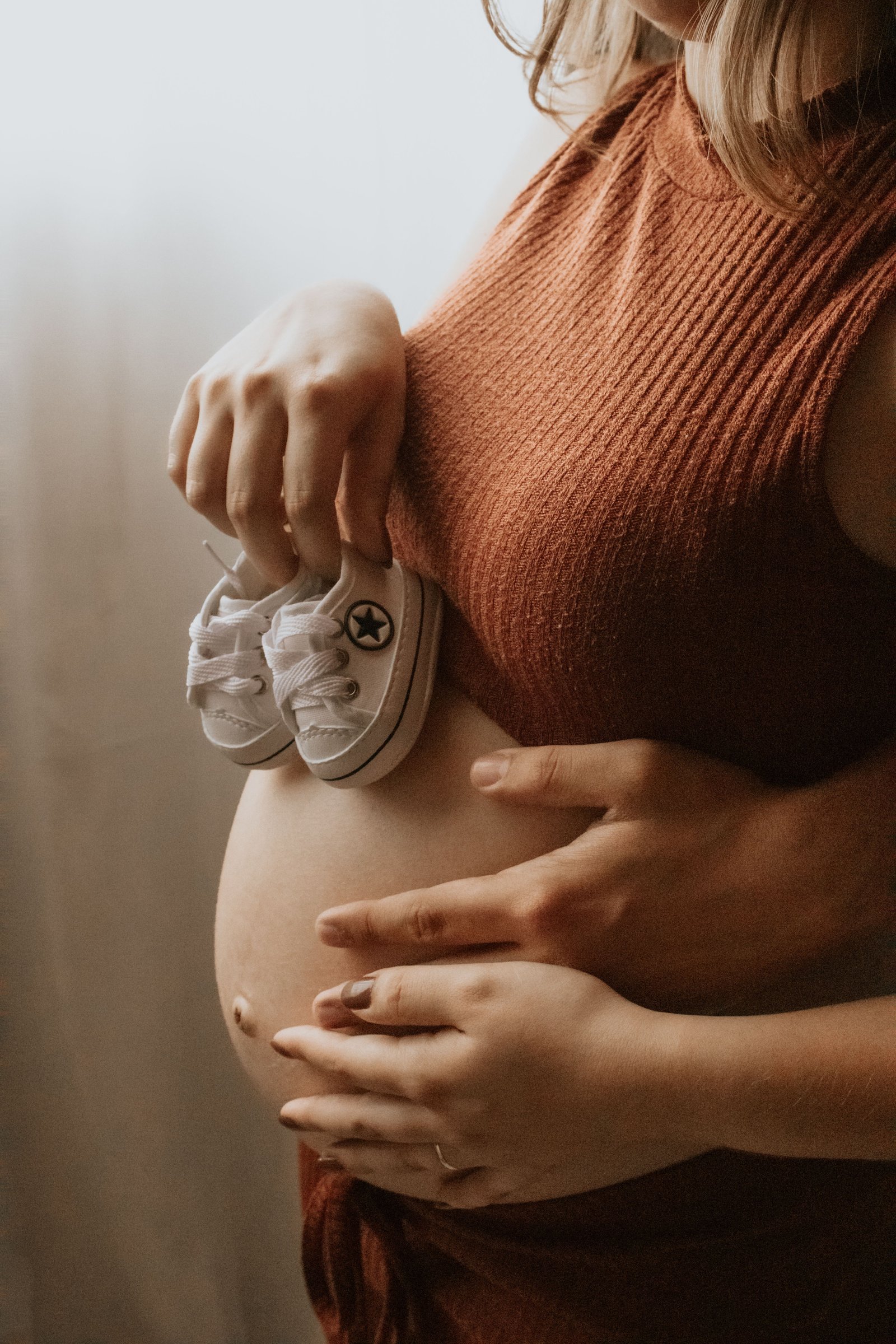 Mujer embarazada sosteniendo zapatos de bebé sobre su vientre